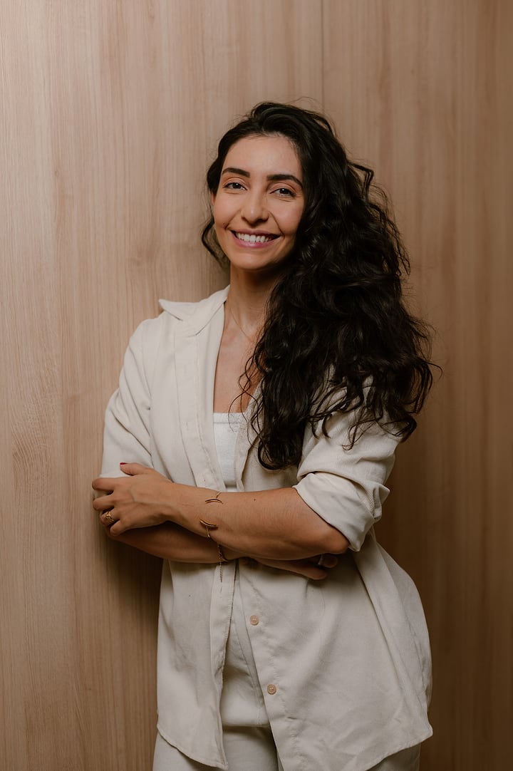 Ana Luiza de camisa branca, de braços cruzados, sorrindo