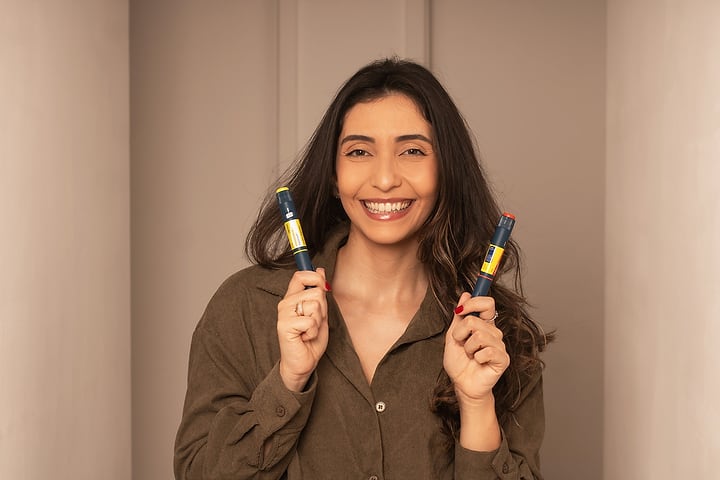 Ana Luiza segurando duas canetas de insulina e sorrindo